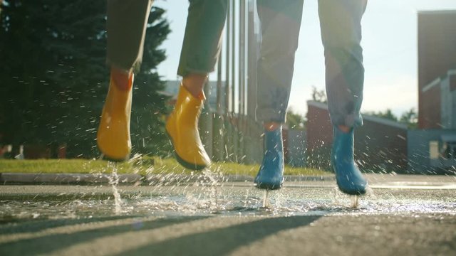 Close-up slow motion of female legs in colorful rubber boots jumping in puddle outdoors having fun on sunny autumn day. Lifestyle and weather concept.
