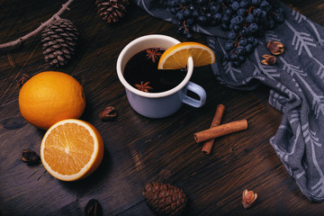 Mulled wine with spices, grapes, pine cones, cinnamon and oranges on a dark wooden background