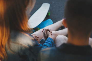 Fototapeta premium a couple of skaters in love is sitting on the curb in the park alley, there are skateboards nearby, no one is visible 1