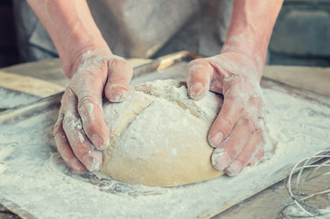 Fototapeta premium The Baker's hands. Process the dough for wheat bread. Rustic style.
