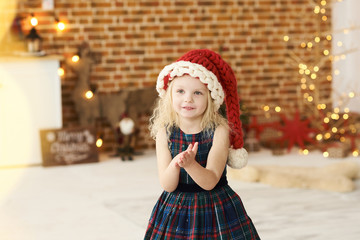 Obraz na płótnie Canvas portrait of a little beautiful girl in christmas hat and dress in christmas decorated room