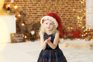 portrait of a little beautiful girl in christmas hat and dress in christmas decorated room