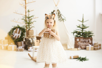 A portrait of a little girl near the wigwam and Christmas tree unpacking Christmas gifts on a white background