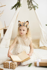 A portrait of a little girl near the wigwam and Christmas tree unpacking Christmas gifts on a white background © jul14ka