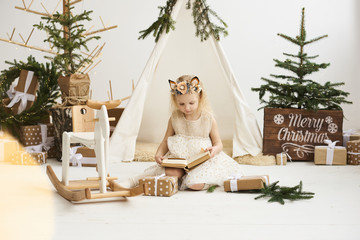 A portrait of a little girl near the wigwam and Christmas tree unpacking Christmas gifts on a white background © jul14ka