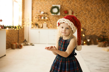 portrait of a little beautiful girl in christmas hat and dress in christmas decorated room