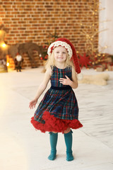 portrait of a little beautiful girl in christmas hat and dress in christmas decorated room