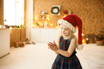 portrait of a little beautiful girl in christmas hat and dress in christmas decorated room