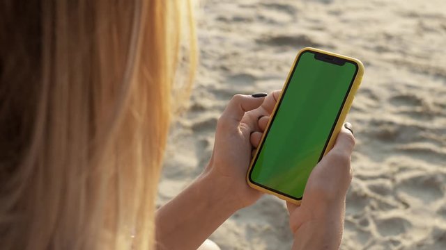 Close up young woman hands use smartphone vertical green screen background sand beach attractive summer technology cellphone chroma key working communication device display sun relaxation slow motion