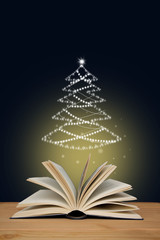 open paper book with magic glow and Christmas tree, concept of magic and mystery, on a wooden table, closeup, copy space