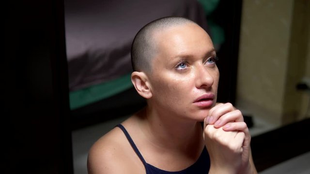 bald woman prays kneeling by the bed in the bedroom. copy space