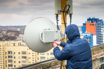  A technician is repairing a wireless data transmitter on the roof of a city building. A man...