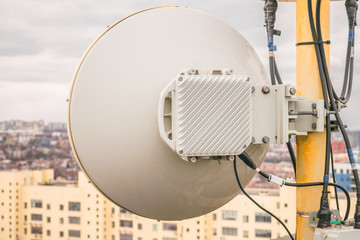 The powerful antenna of the radio relay base station of mobile communication is close-up. There is a wireless data transmitter on the roof of a city building. Telecommunication concept.