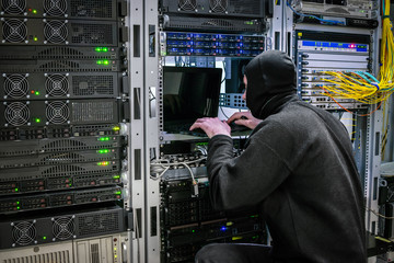 hacker is looking for vulnerabilities in the protection of  server room. Virus DDoS attack computer servers data center. Criminal steals information from the database of the modern computer center. 