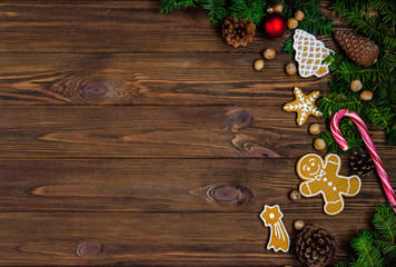Bright Christmas or New Year wooden wooden background with fir branches, Christmas decorations, Christmas gingerbread cookies, nuts, dried orange slices, pine cones.