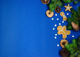 Bright Christmas or New Year blue background with branches of spruce, Christmas gingerbread cookies, marshmallows, dried orange slices, pine cones.