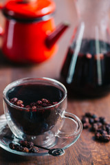 Winter berry tea with cranberries, apple, cinnamon, black mulberry, lemon, honey and thyme in a glass cup on wooden table. Horizontal, closeup view