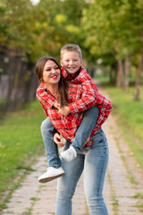 Fototapeta premium Mom, smiling, holds on her back a laughing son.