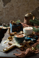 christmas still life with two cups of hot creamy drink (cocoa, chocolate, coffee) with snowflake cocoa ornament on top stands on wooden boards on rustic table with fir tree, spices