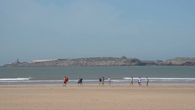 ESSAOUIRA, MOROCCO, MARCH 14, 2014. The sand bech with boys playing football  on a sunny day with a blue sky, in Essouira Morocco, on March 14th, 2014.