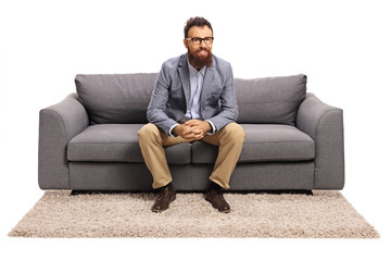 Bearded guy with glasses sitting on a gray sofa