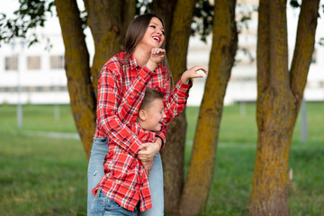 Mom, laughing cheerfully, hugs her son, who squinted and raised his hands up.