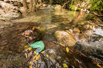 Abandoned garbage on the shore of a stream of clean water.