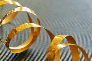 Golden curly ribbon on dark background. Serpentine with curls for use as a christmas, anniversary, marriage, wedding or celebration background with copy space.