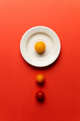 three cherry tomato, one on white plate, two on a table