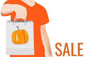 Young man holding shopping bag with drawing pampkin on it. Person showing a sign Sale on bag, board, banner in hand. Modern lifestyle, new purchase. Mockup.