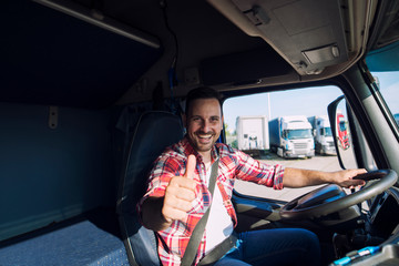 Portrait of professional motivated truck driver holding thumbs up in truck cabin. Transportation service.