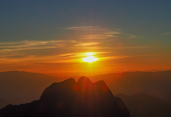 The high mountains of Chiang Dao in Chiang Mai, Thailand, as the sun sets behind the mountain peaks, the clouds in the sky are golden, red, orange, and yellow.