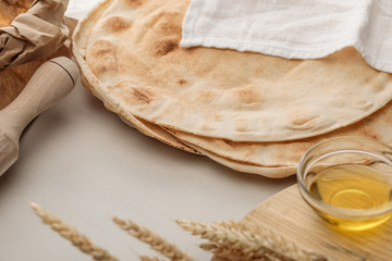 flat lavash bread covered with white towel near rolling pin and cutting board with spikes and oil