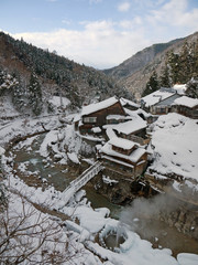 Beautiful Japanese Satoyama winter  mountain range scenery with mountain river, bridge, small house and village on hill slope with pine forest in snow in Nagano prefecture Yudanaka snow monkeys park