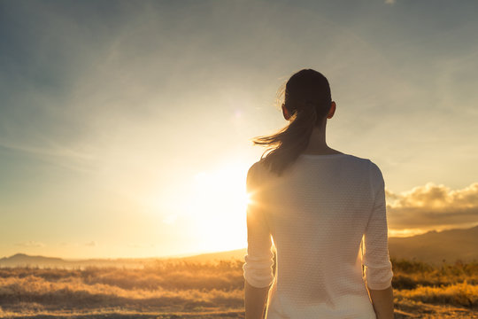 Life is beautiful. Woman standing facing a beautiful golden sunrise. 