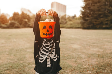 Kid in skeleton outfit standing with Jack or lantern bucket