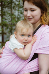 Young redhead babywearing mother carry her sleepy one year old baby girl in a pink wrap sling 