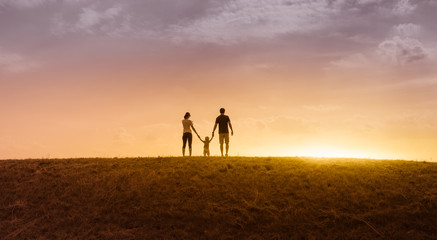 Family of three holding hands walking together at sunset. 