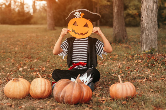 Funny kid with pumpkins and paper mask