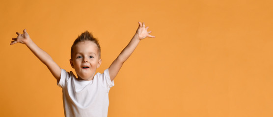 Young boy kid in white t-shirt celebrating happy smiling laughing with hands spreading up on yellow - 293251600