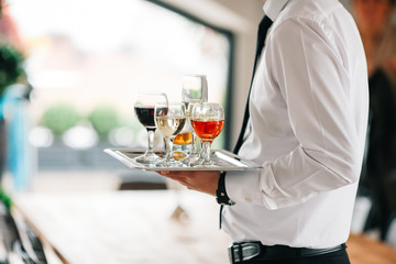 Waiter serving glasses of cold beer, soft drinks and white wine on the tray at a business meeting
