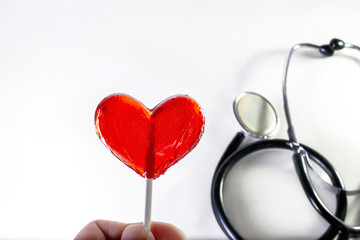 red heart-shaped Lollipop close-up, medical stethoscope on white background
