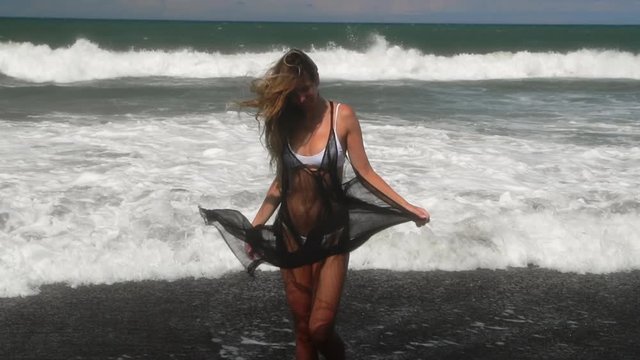 Beautiful young woman in white bikini and light black summer dress. Fitness healthy active living. Sport and travel. Weight loss and body image concept. Girl with perfect fit body on tropical beach.