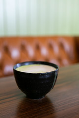 Golden milk matcha latte with turmeric, on coffee shop table, leather chair and green wall in background, copy space
