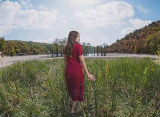 a beautiful, young brown-haired woman in a red dress on the background of a morning lake with cypresses, a girl with a slender figure posing against nature