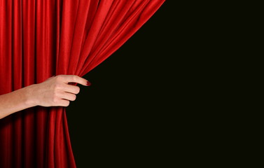 Hand opening red curtain over black background
