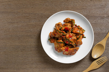 top view of stir fried chicken with red curry paste in a ceramic dish on wooden table. hot and...