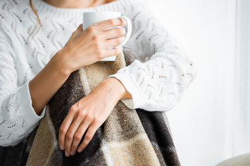 cropped view of woman with blanket in white sweater holding cup