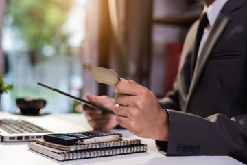 Male businessmen use credit cards to conduct financial transactions through tablet in office.