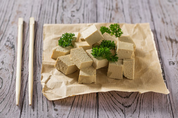 Pieces of tofu with greens on paper and chopsticks. Soy cheese.